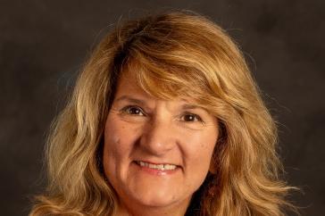 Headshot of Patricia Halpin, who has shoulder-length blonde hair and is wearing a bright pink jacket and necklace